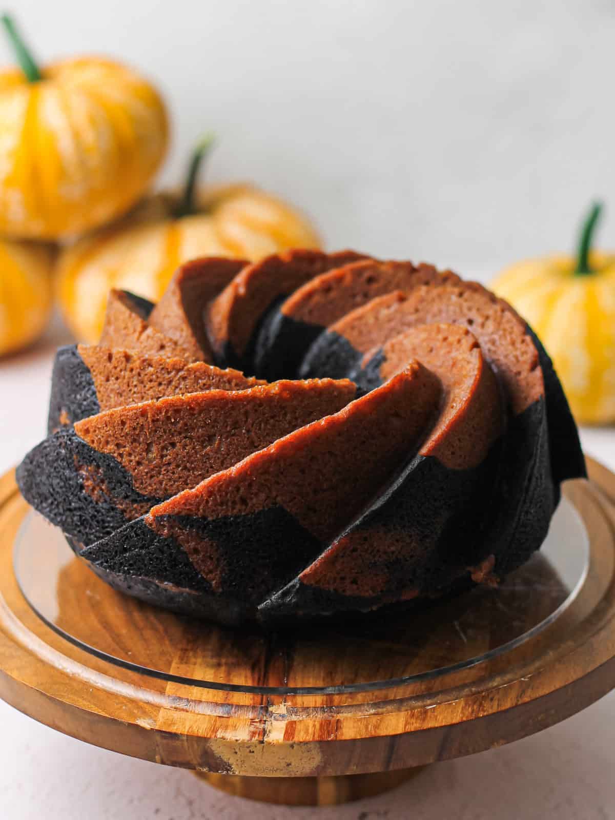 Whole marbled pumpkin Bundt cake on a cake stand with small pumpkins in the background.