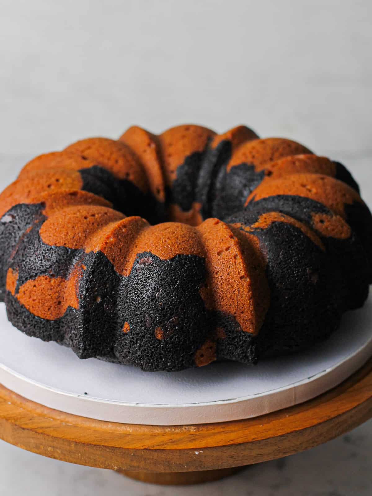 Cake stand holding an orange and black swirled Bundt cake, baked in a Nordicware Bundt pan that holds 12 cups of batter.