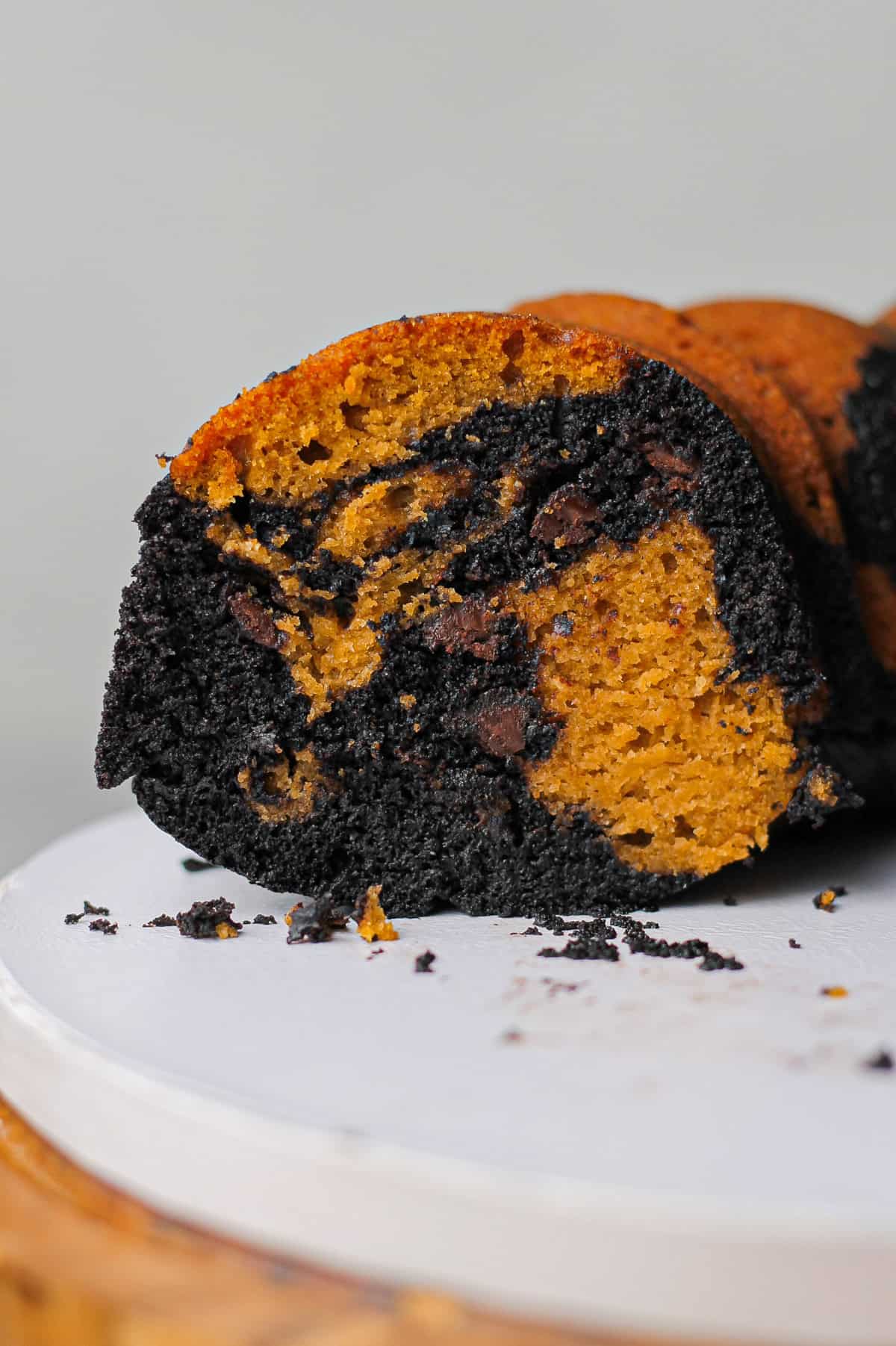 View of the inside of the pumpkin and black cocoa Bundt cake, with a slice removed to reveal the marbling and chocolate chips added to this version.