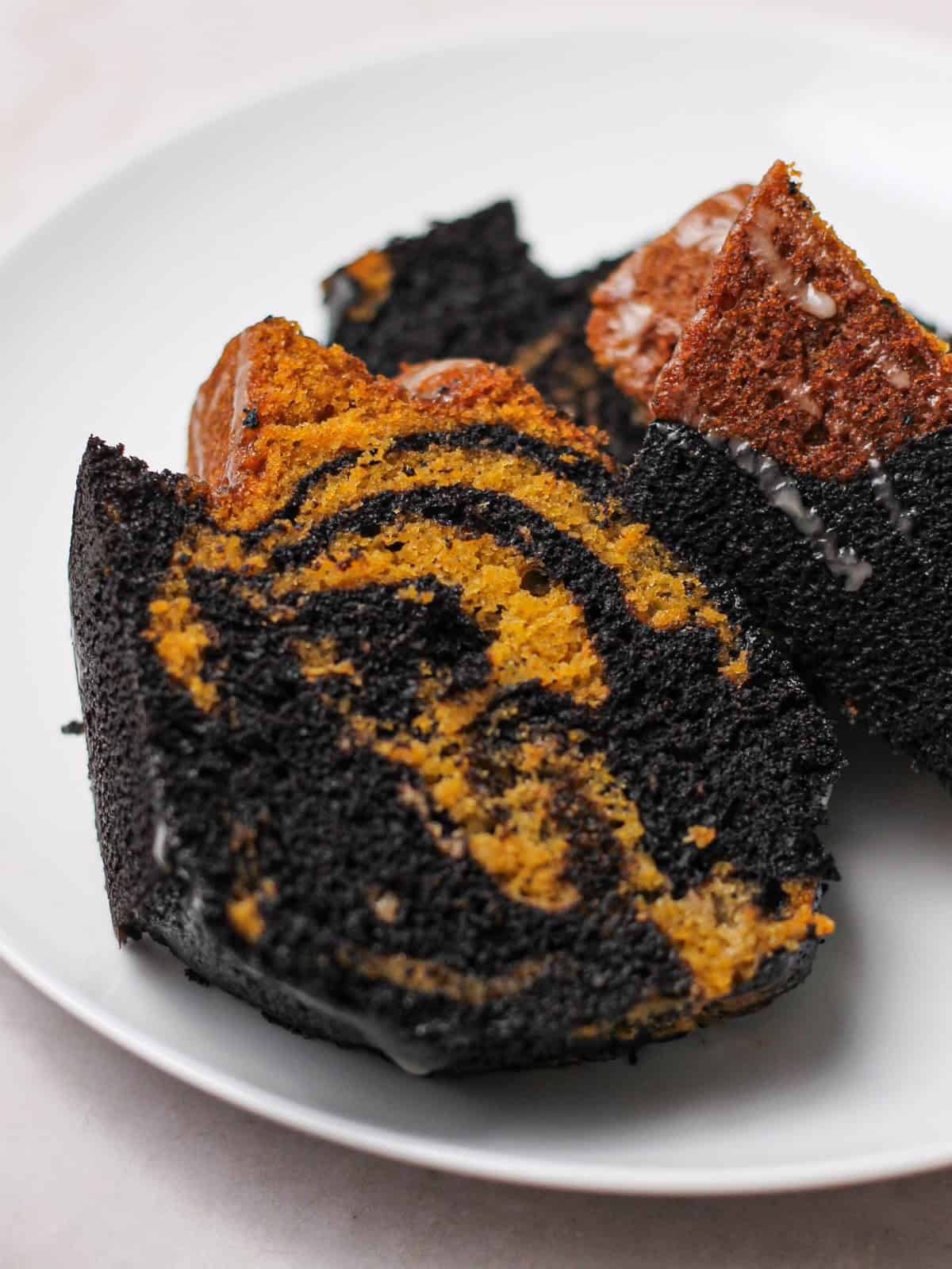 Slices of marbled pumpkin and black cocoa Bundt cake on a white plate.